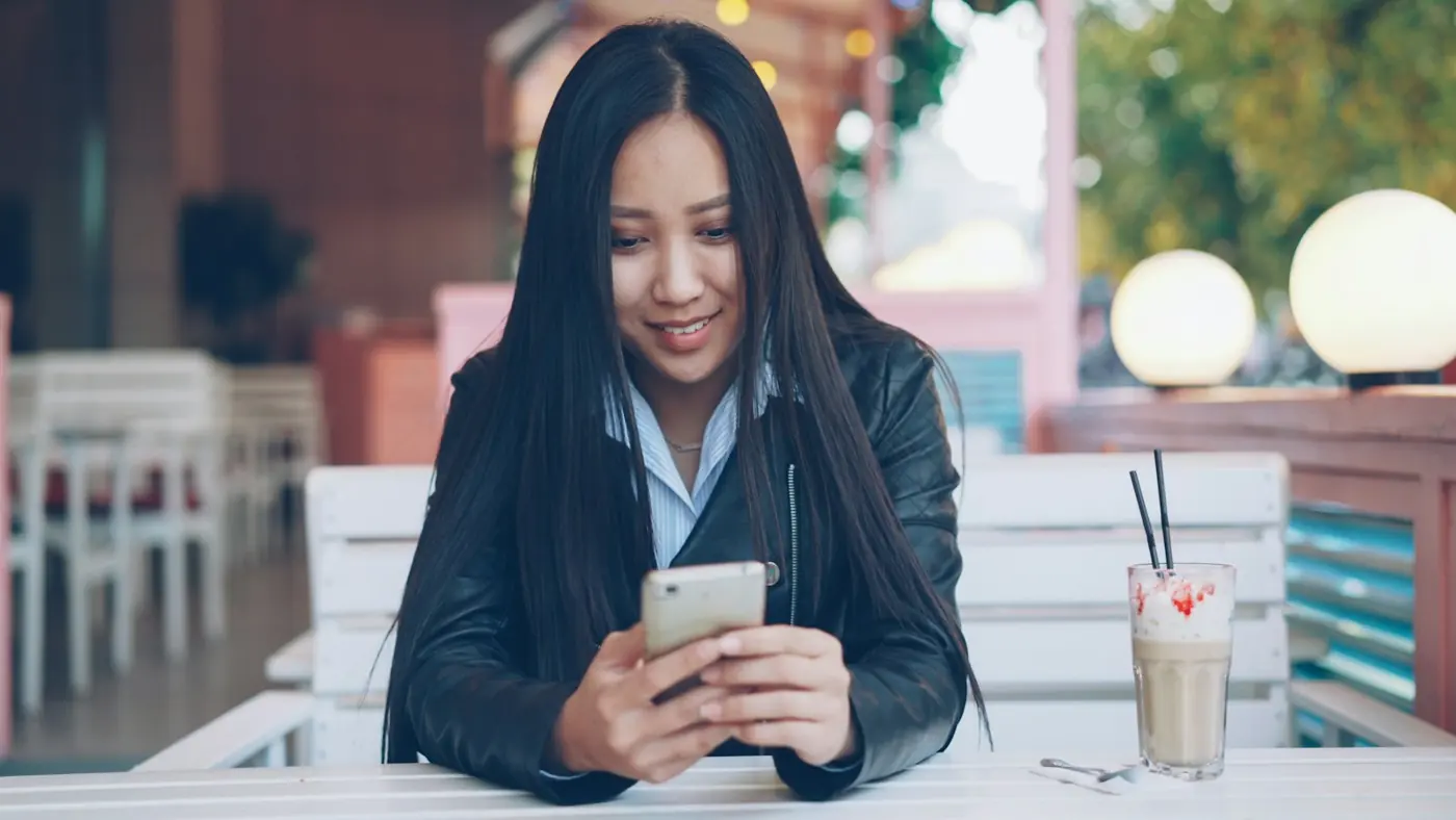A young woman smiling at her phone at a café table
